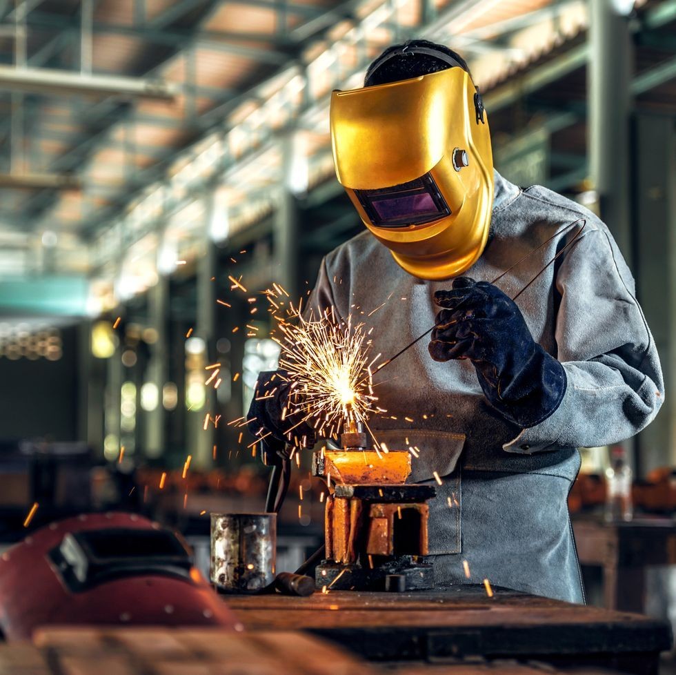 Welder in protective gear performing metal fabrication with sparks in a manufacturing workshop