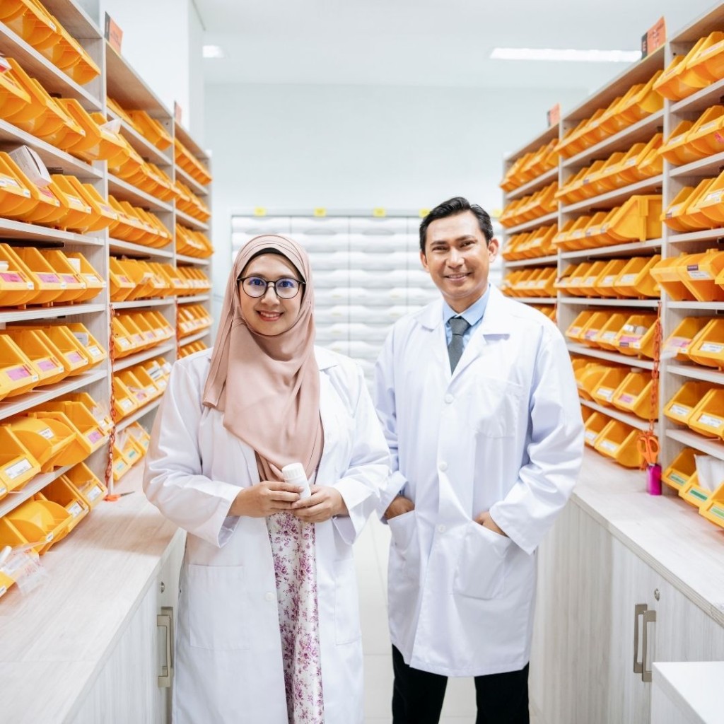 Pharmacy professionals in lab coats managing medical inventory in a stocked dispensary aisle