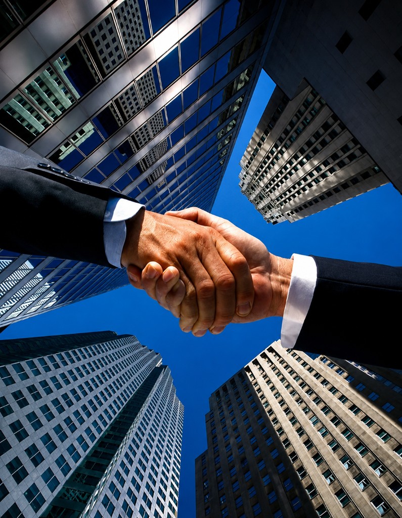 Business handshake against commercial skyscrapers representing property deals in Bahrain and Saudi Arabia